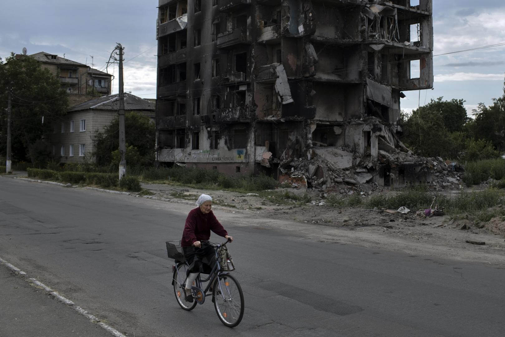 ESCOMBROS. Una mujer mayor pasa en bicicleta junto a los restos de un edificio de apartamentos cerca de Kiev.