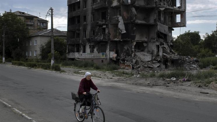 ESCOMBROS. Una mujer mayor pasa en bicicleta junto a los restos de un edificio de apartamentos cerca de Kiev.